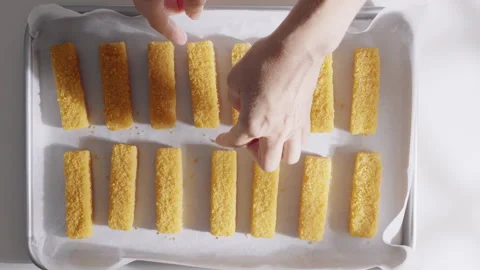 Hands arrange breaded fish sticks on a parchment lined baking tray before oven c Stock Footage 333331160