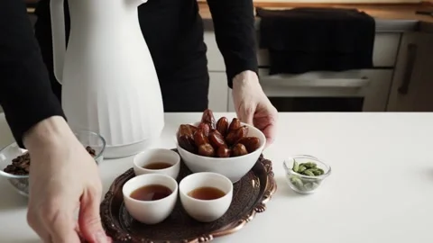 Hands arranging a bowl of dates and white finjan cups on ornate serving tra.. Stock Footage 332159786