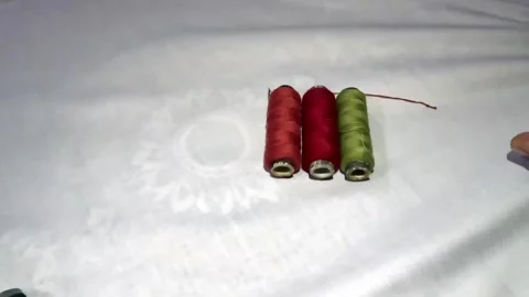 Hands Arranging Colorful Sewing Thread Spools in a Row on White Fabric 库存影片 341762568