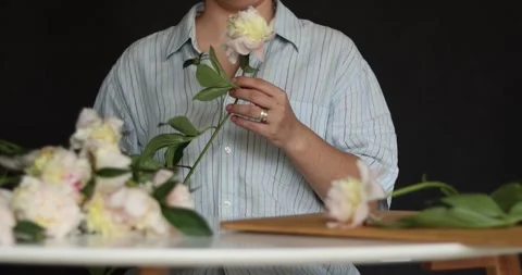 Hands arranging delicate white and pink peonies on a wooden surface Stock Footage 339078805