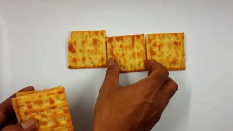 Hands arranging golden square crackers on a clean white surface for a snack Video stock 322997358