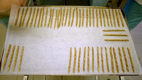 Hands arranging grissini breadsticks on a baking tray with parchment paper in a Stock Footage 332922312