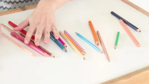 Hands arranging scattered children’s colored pencils on white table Stock Footage 331514307