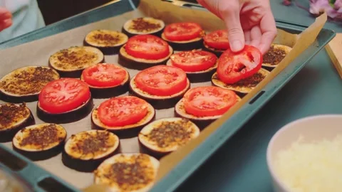 Hands arranging sliced tomatoes on eggplant in kitchen from above Видео 342868191