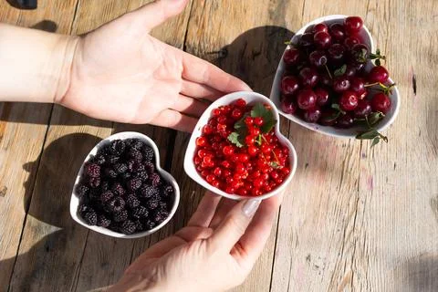 Hands arranging three heart shaped bowls of fresh cherries, redcurrants and.. Stock Photos