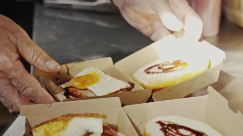 Hands assembling and packing fresh bacon and egg rolls into cardboard takeaway 動画素材 332617546