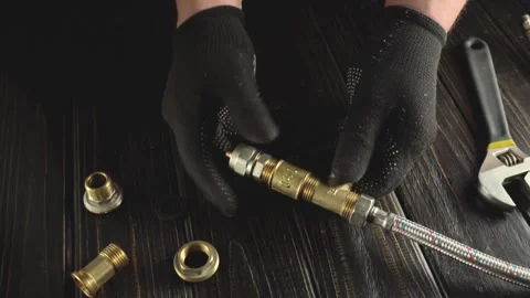 Hands assembling brass plumbing fittings with gloves on a wooden work surface, Stock Footage 338306643