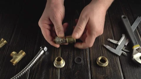 Hands assembling brass plumbing fittings with tools on wooden work surface, Stock Footage 339320438