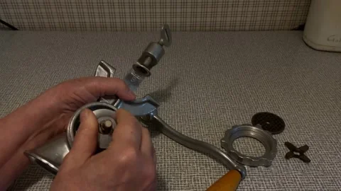 Hands assembling metal meat grinder parts on textured fabric surface, with .. Stock Footage 347977730