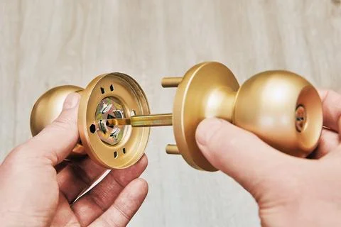 Hands assembling new brass-colored door knob on wood background. Stock Photos