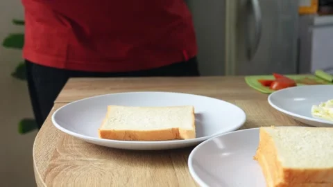 Hands assembling sandwich by layering crisp lettuce, sliced tomatoes, and fried Stock Footage 327636111