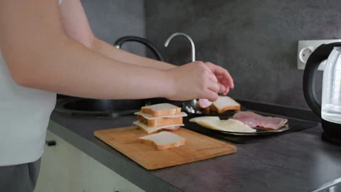 Hands assembling stack of sandwiches using slices of bread, ham, and cheese on Stock Footage 317926953
