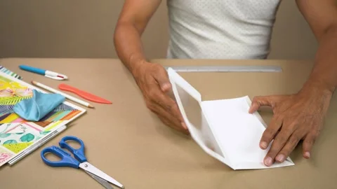 Hands assembling white cardstock frame with craft tools and patterned paper Stock Footage 345617077