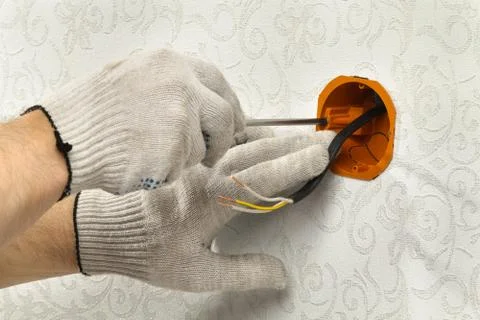 Hands attach the socket box to the wall to place the electrical outlet Stock Photos