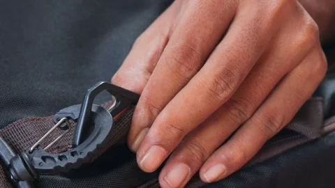 Hands attaching a plastic strap hook to a backpack strap Stock Footage 339044333