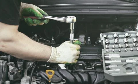 Hands of an auto mechanic with a socket wrench in the engine compartment of a Stock Photos