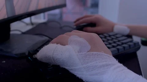 With hands bandaged and a focused expression, typing on a keyboard set against a Stock Footage 297202535