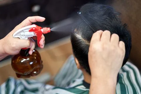 Hands of a barber using a water dispenser to wet a customer's hair Stock Photos