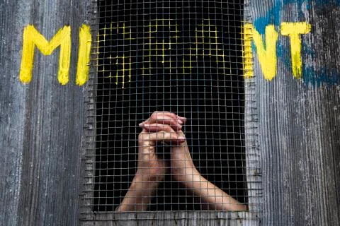 Hands behind bars graffiti reading migrant support for refugees Stock Photos