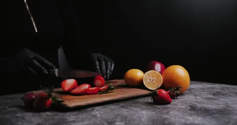 Hands in black gloves cut juicy fresh strawberries on black kitchen table. Video stock 148246169