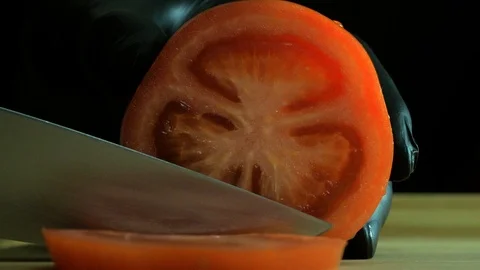Hands in black gloves cut a tomato on the board on a black background Vídeo Stock 112002606