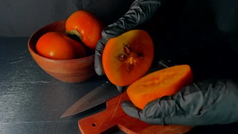 Hands in black gloves holding halved juicy persimmon. Fresh fruit on cutting Video stock 325956550
