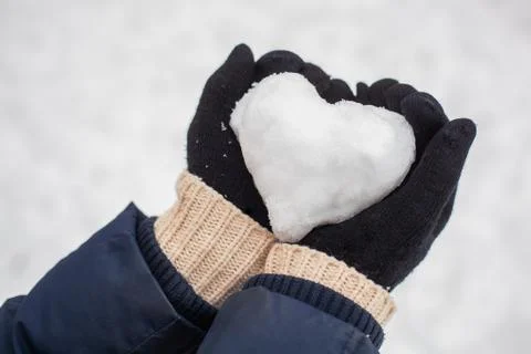 Hands in black gloves keep the snow folded in the shape of a heart against th Stock Photos