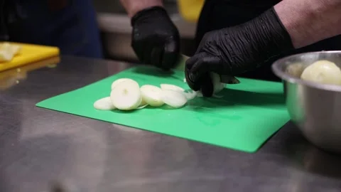 Hands in black gloves slice white onion rounds on green board Stock Footage 337582309