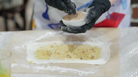 Hands in black gloves sprinkles nuts on the dough. Cook woman prepares fresh Stock-Footage 132031730