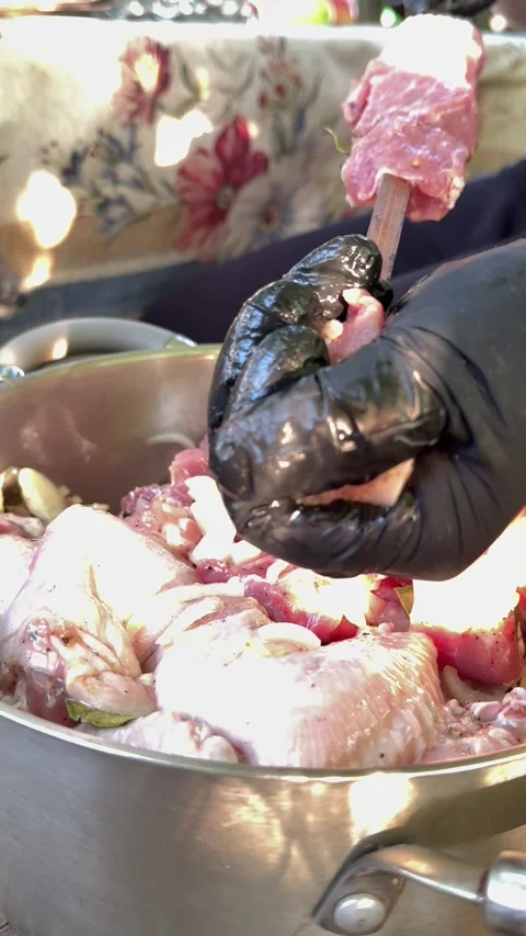 Hands in black gloves threading marinated pork and chicken wings onto metal Stock Footage 345182714