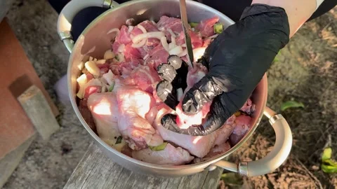 Hands in black gloves threading marinated pork and chicken wings onto metal Stock Footage 345183457