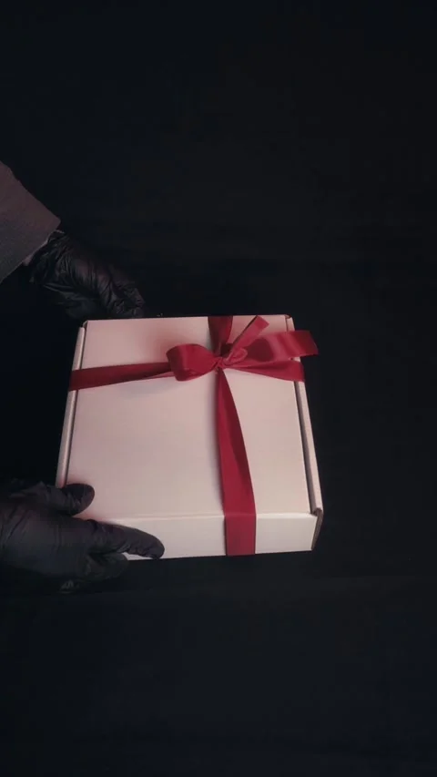Hands in Black Gloves Tying Red Ribbon on White Gift Box Dark Background Video stock 323453388