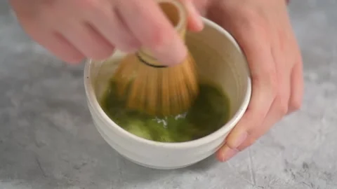 Hands blending with a bambu chasen in a white bowl some green tea matcha Stock Footage 141127109