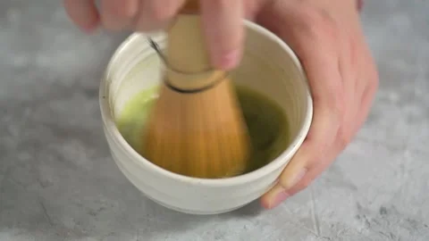 Hands blending with a bambu chasen in a white bowl some green tea matcha Stock Footage 141127158