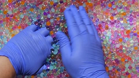 Hands in blue gloves are immersed in a pile of multicolored hydrogel small balls Stock Footage 277438246