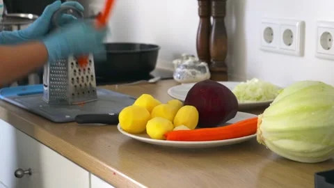 Hands in Blue Gloves Grating Fresh Carrot on Metal Grater in Home Kitchen Stock Footage 348005086