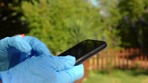 Hands in blue gloves holding a smartphone outdoors in garden. Man using a phone. Stock Footage 313298829
