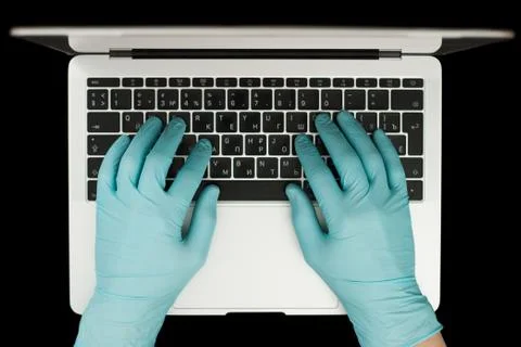 Hands in blue protective gloves typing on laptop keyboard. Top view. Coronavi Stock Photos