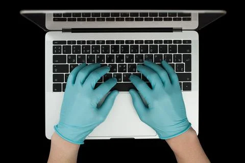 Hands in blue protective gloves typing on laptop keyboard. Top view. Coronavi Stock Photos