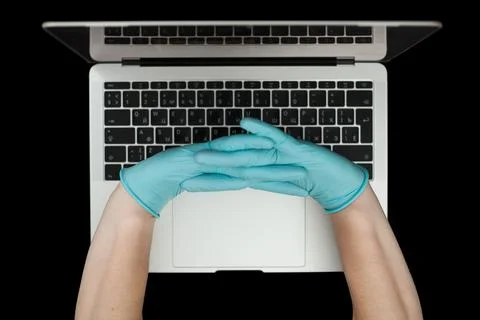 Hands in blue protective gloves typing on laptop keyboard. Top view. Coronavi Stock Photos