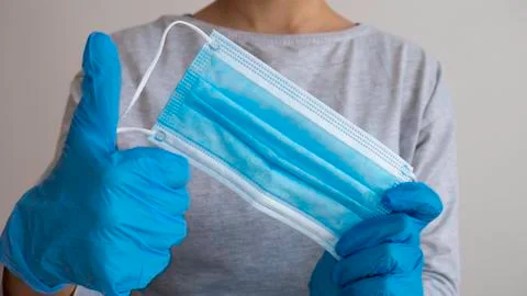Hands in blue rubber gloves hold a medical mask with thumbs-up. Foto stock