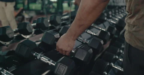 Hands bodybuilder picking up or choosing dumbbell that are weights suitable Stock Footage 156368688