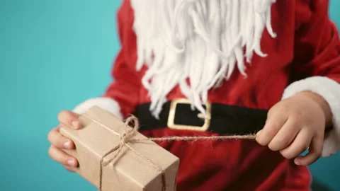 Hands of boy in Santa's costume pulling on string of wrapped gift box. Child Stock Footage 228723580