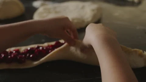 The hands of a boy trying to glue the dough filled with cherry jam to make pies Stock Footage 246648810
