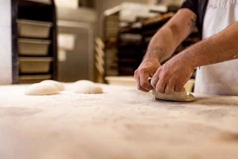Hands of bread baker kneading fresh and uncooked bread dough on table during  写真素材