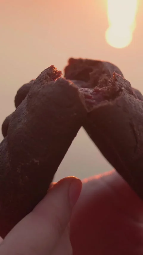 Hands break dark small rye pie with cherry filling in half near river at sunset. Stock Footage 269540113