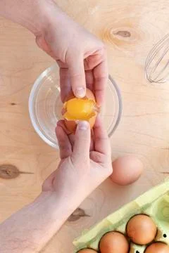 Hands break a raw egg. Stir the protein with the yolk. Glass bowl on a wooden Stock Photos