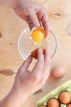 Hands break a raw egg. Stir the protein with the yolk. Glass bowl on a wooden 库存照片