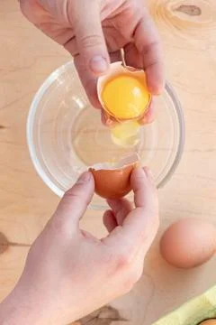 Hands break a raw egg. Stir the protein with the yolk. Glass bowl on a wooden Stock Photos