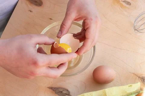 Hands break a raw egg. Stir the protein with the yolk. Glass bowl on a wooden 库存照片